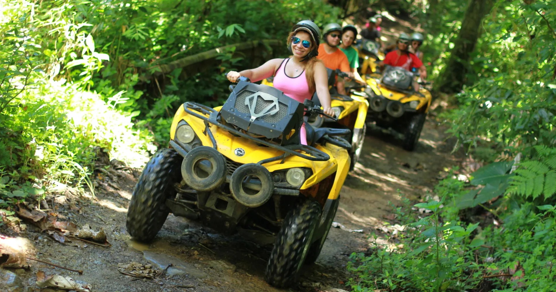 Four people riding yellow ATVs on a forest trail.