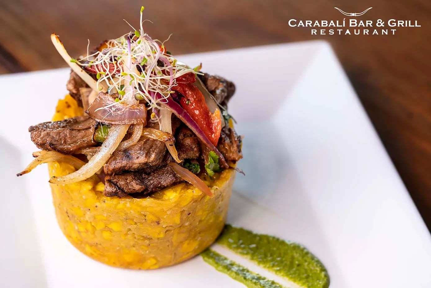 Gourmet dish with meat, onions on a corn base, garnished with sprouts and sauce on a square plate.