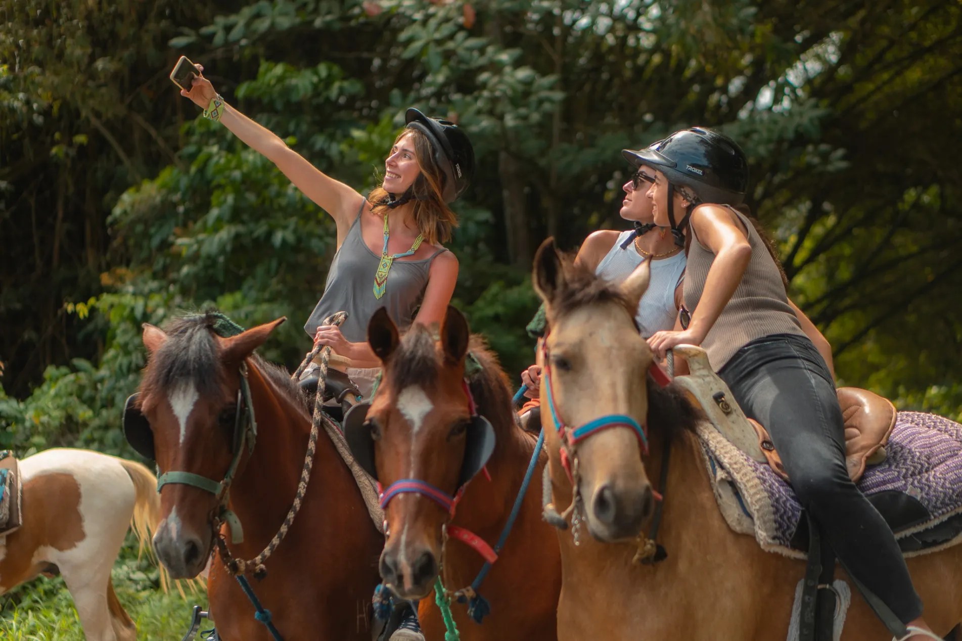 Two people on horses taking a selfie in a forested area.
