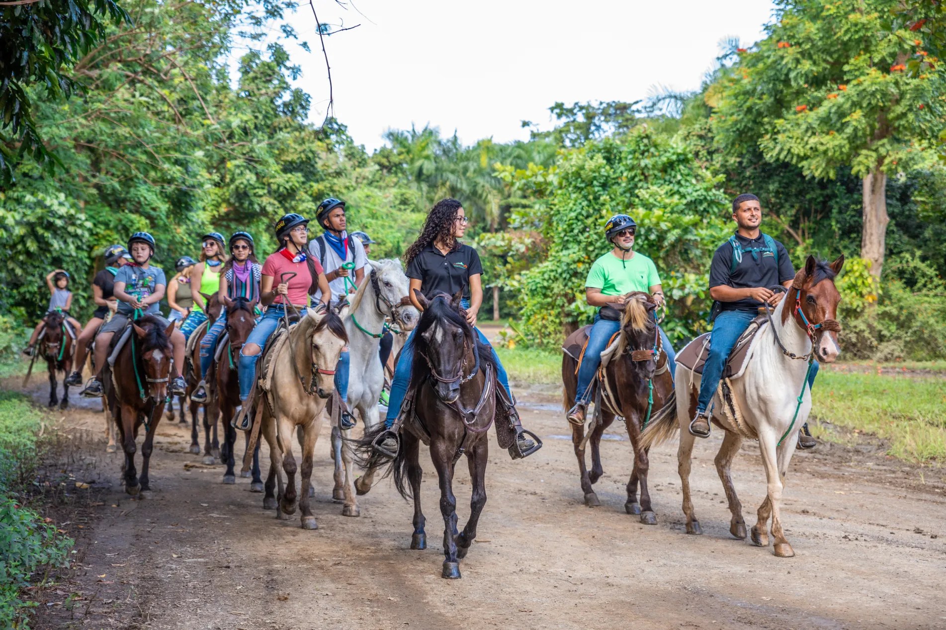 Group of people horseback riding on a dirt path surrounded by lush greenery.