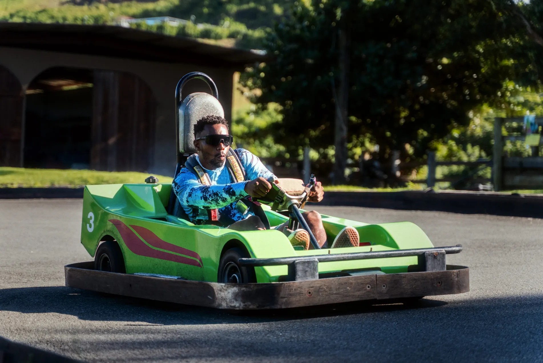 Person driving a green go-kart with number 3 on a sunny track.