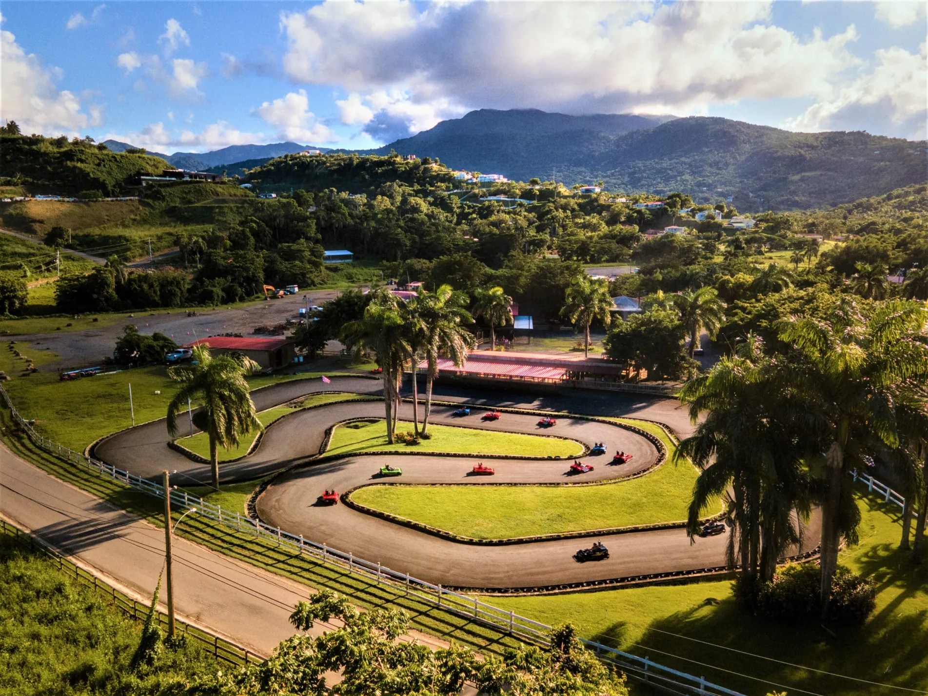 Aerial view of a go-kart track surrounded by palm trees and mountains in the background.