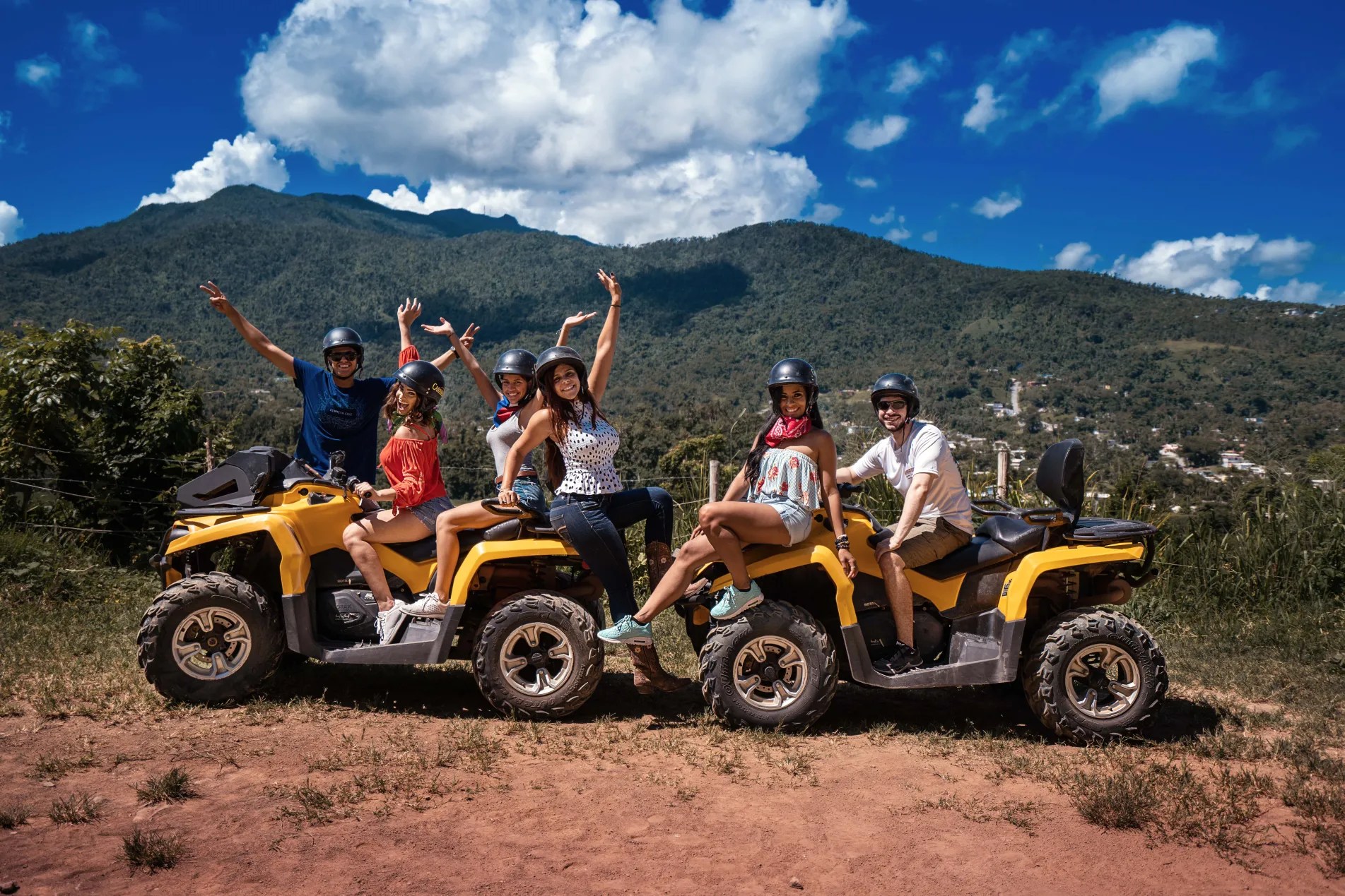 Group on ATVs in outdoor setting with mountains and blue sky in the background.
