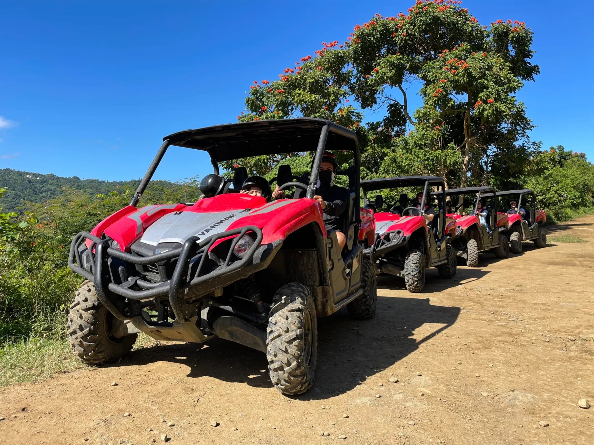 Four red off-road vehicles parked on a dirt path with trees in the background.