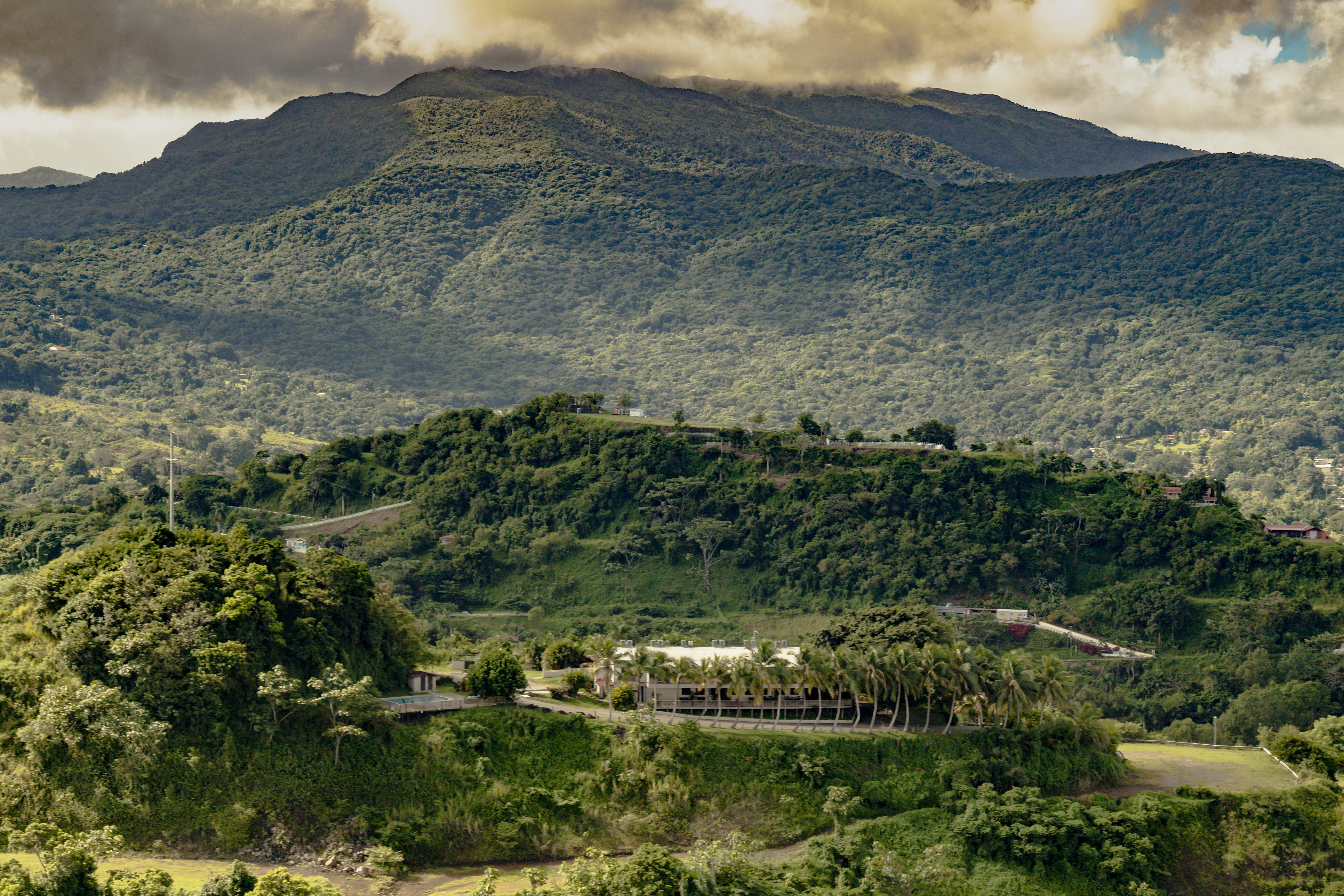 Lush green hilly landscape with a cloudy sky and a small structure at the foreground.