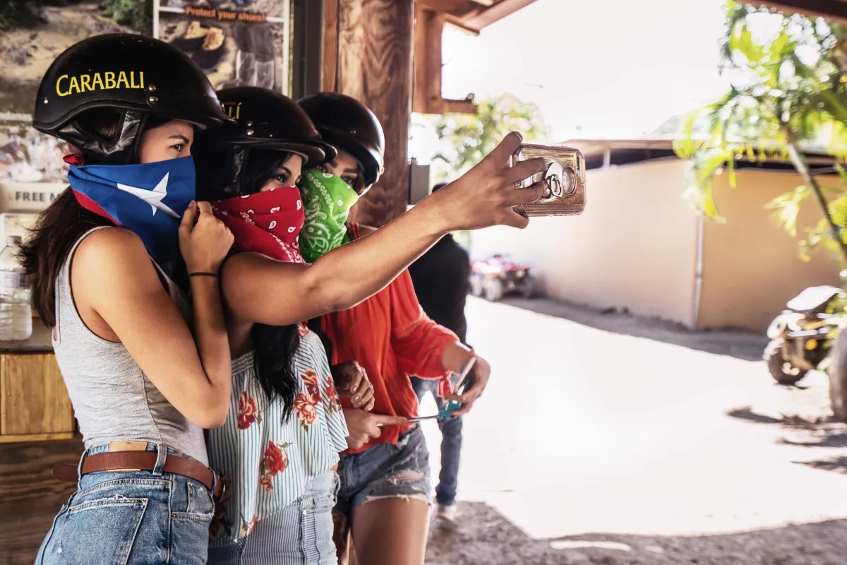 Three people in helmets and bandanas taking a selfie outdoors.