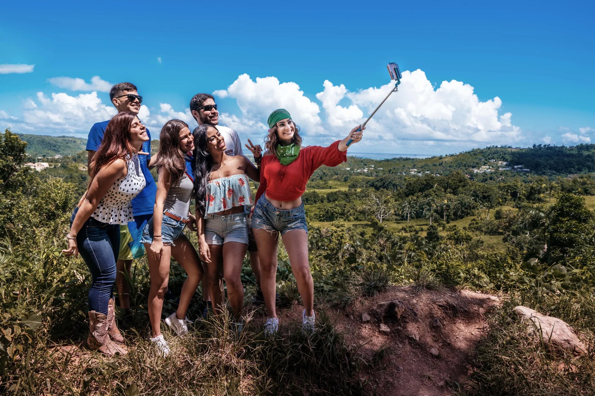 Group of friends taking a selfie with a selfie stick in a hilly landscape on a sunny day.
